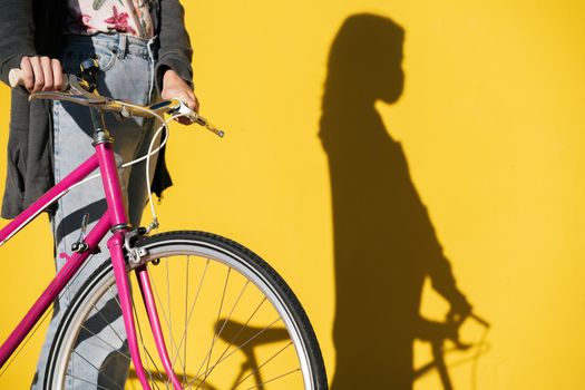 unrecognizable woman wearing mask with retro bike and her shadow on a colorful yellow wall, concept of protection against covid and sustainable mobility, copy space for text