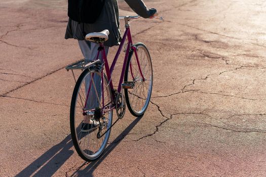 unrecognizable young woman walking with her retro bike at sunset, concept of active lifestyle and sustainable urban mobility
