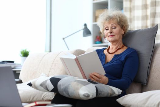 Elderly woman is reading book at home on couch. Home leisure pensioners concept