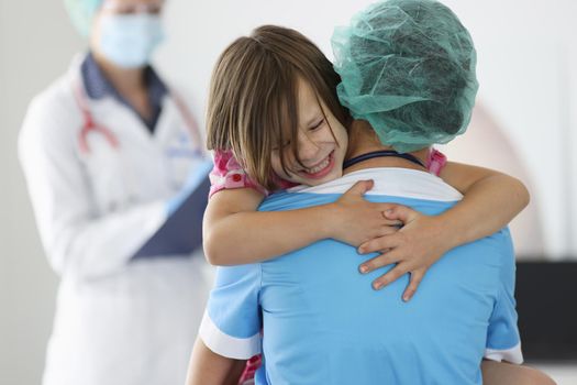 Doctor holds frightened little child girl in arms in clinic. Children fear of injections concept