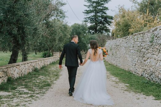 Happy stylish smiling couple walking in Tuscany, Italy on their wedding day. The bride and groom walk down the street by the hands. A stylish young couple walks. Husband and wife communicate nicely. Lovers run through the streets of the city.