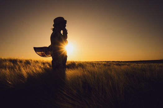Female farmer is standing in her wheat field and enjoying sunset.