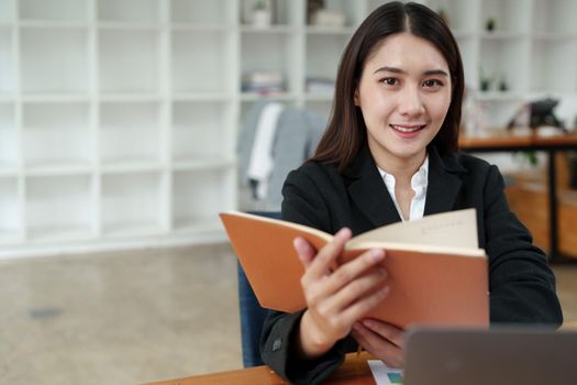 Portrait of a beautiful Asian businesswoman in a formal suit sits at her office desk with using notebook and laptop computer in office.