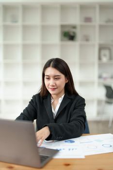 Portrait of a beautiful Asian businesswoman in a formal suit sits at her office desk with using laptop computer in office.
