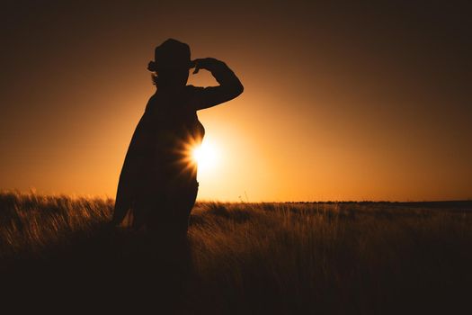 Adult woman is cultivating barley on her land. She is enjoying sunset in her field.