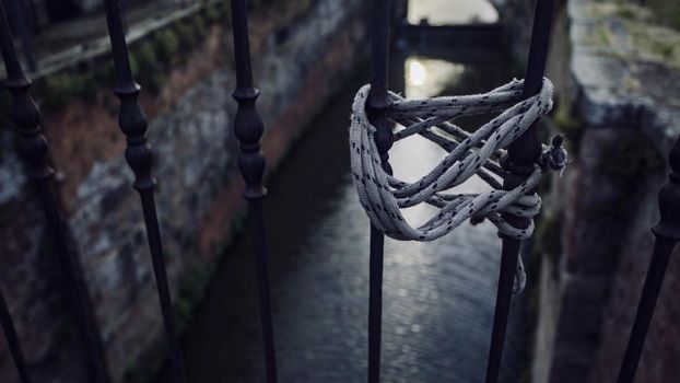 A lanyard tied to a handrail against a canal in the background - White rope tied