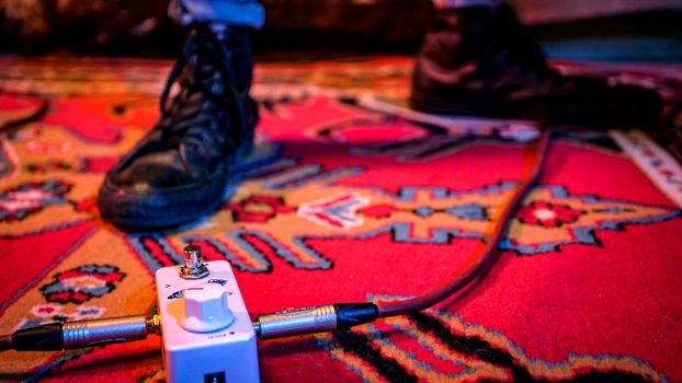 Male guitarist with black boot switches effects pedal to change his guitar sound