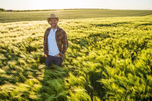Farmer is cultivating barley. He is smiling and looking at camera while standing in his barley field.