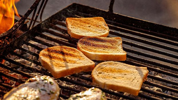 Pieces of white bread are grilling on the open fire outside, grill and barbecue, bbq at the countryside, cooking food, cooking on the fire, flame and coal