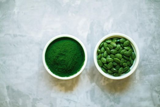 spirulina powder and tablets in white plates on concrete background. top view
