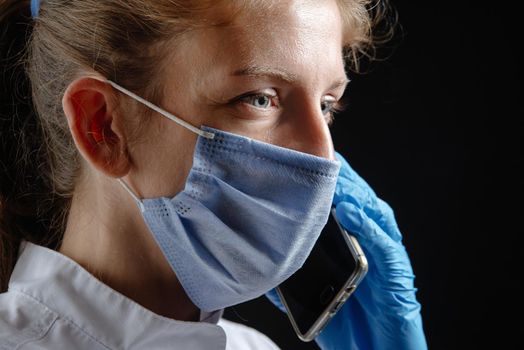 The doctor speaks on the phone against a black background. A female doctor or nurse is giving advice over the phone. A health care worker answers the phone. Closeup