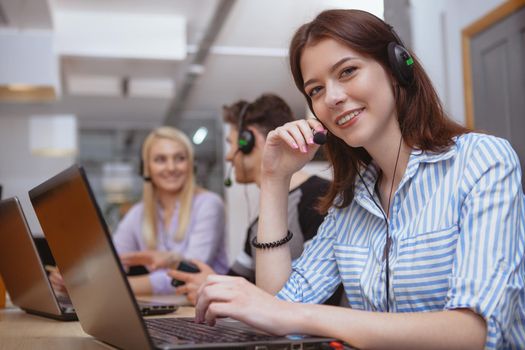 Attractive cheerful female call center worker wearing headset with microphone smiling to the camera. Lovely woman enjoying working at customer support service, smiling to the camera, copy space