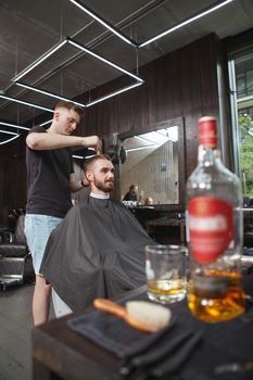 Vertical shot of a professional barber giving a new hairstyle to his male client