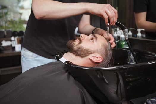 Unrecognizable barber washing hair of male client prior to haircut