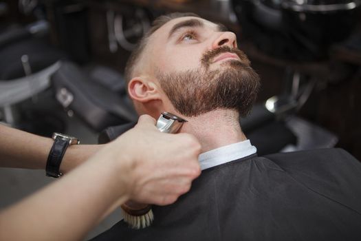 Cropped shot of a barber using electric clipper on the beard of male client