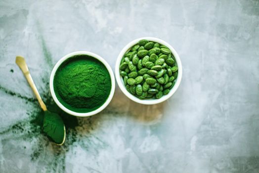 spirulina powder and tablets in white plates on concrete background. top view