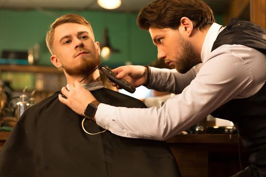 Young man having his beard shaved and trimmed by a professional barber at the barbershop service client customer consumerism luxury wellbeing comfort barbering professionalism hipster.