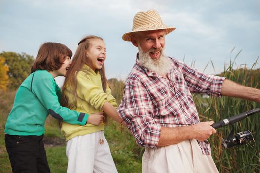 Cheerful senior fisherman laughing to the camera while fishing with his grandkids on the lake