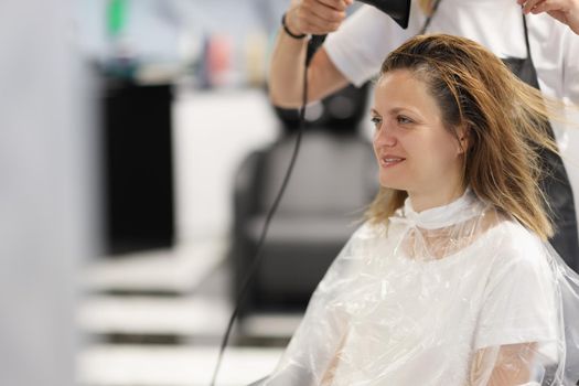Hair styling process in beauty salon with hair dryer. Hairdresser drying wet hair to woman with hair dryer in barbershop