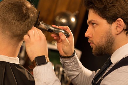 Cropped close up profile shot of a handsome young professional barber looking concentrated giving a haircut to his customer using clipper trimmer equipment hairstyling barbering work barbershop.