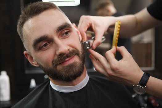 Handsome man smiling while barber trimming his beard