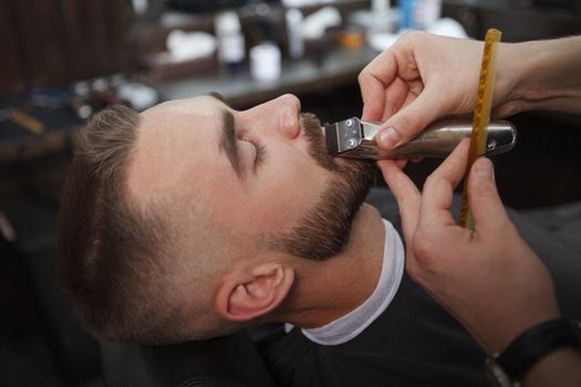 Unrecognizable barber usingelectric clipper, trimming moustache of a male client