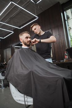 Vertical shot of a handsome man getting a new hairstyle by professional barber at barbershop