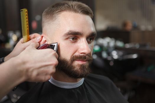 Close up of a handsome bearded man getting his hair trimmed by professional barber