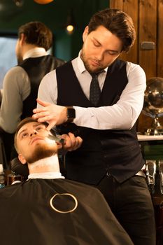 Vertical shot of a handsome professional barber working shaving his client at the barbershop occupation razor equipment barbering job lifestyle hipster traditional hairdresser stylist.