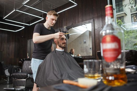 Professional barber looking concentrated, cutting hair of a male client, copy space