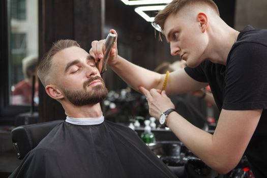 Handsome man looking relaxed while getting his beard trimmed by barber