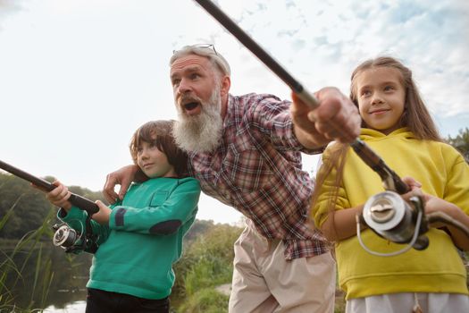 Low angle shot of senior fisherman and his rtwo grandkids fishing together