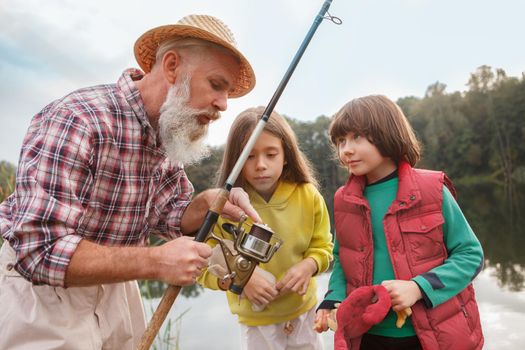 Senior man teaching his grandchildren fishing, showing them spinning rod