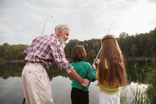 Rear view shot of a senior fisherman teaching his grandkids fishing on the lake