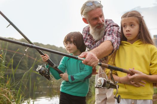 Happy senior man enjoying teaching his grandkids fishing on the lake