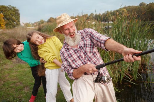 Two children and their grandpa pulling big fish together out of the water