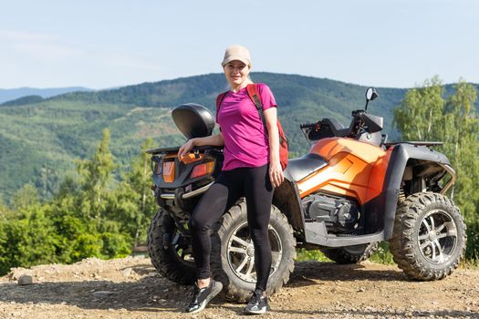 Smiling happy woman riding quad bike on a sunny day, against blue sky. Low angle shot. Freedom, happiness, nature concept.