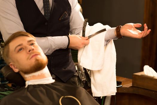 Cropped shot of a professional barber wiping shaving cream off the razor while shaving his male customer working at the barbershop occupation professionalisme experience service work job.