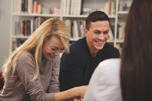 Happy college friends laughing joyfully, talking at the campus library. Cheerful male student having fun with his friends at school. Communication, lifestyle, education concept