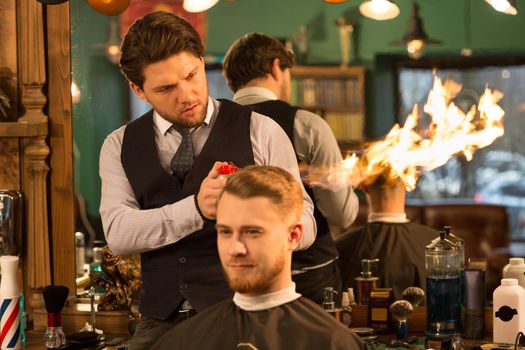 Professional handsome bearded barber giving a haircut to his male client hair fire treatment service masculinity hapster vintage extreme dangerous flames burning experience hairdressing salon.