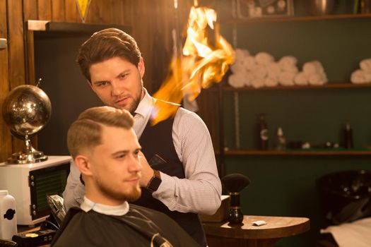 Handsome professional barber smiling giving hair fire treatment to his handsome male customer copyspace extreme technology unusual hairdresser styling hairstylist split ends service barbering barbershop.