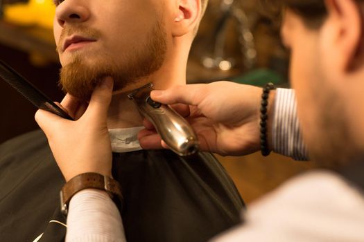 Cropped close up of a bearded man having his beard trimmed by a professional barber using trimmer clipper barbershop styling masculinity hipster service job customer client shaving barbering.