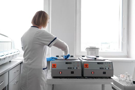 Back of a female blonde doctor using the reaction vessel of a centrifuge in a hospital