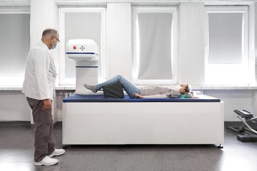 Female patient lying on a stretcher of a x-ray machine next to a female doctor with mask