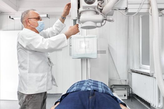 Doctor with mask working with an x-ray machine with a patient in an hospital