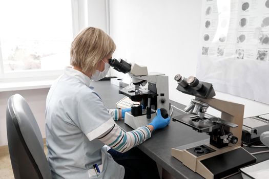 Female lab technician using a microscope in an hospital room