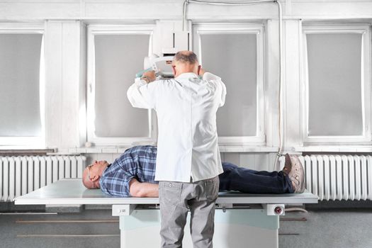 Doctor preparing a x-ray machine to use it with a patient that is lying on a stretcher