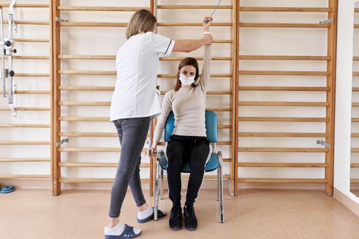 Physiotherapist rehabilitating a patient sitting in a chair in a room of an hospital