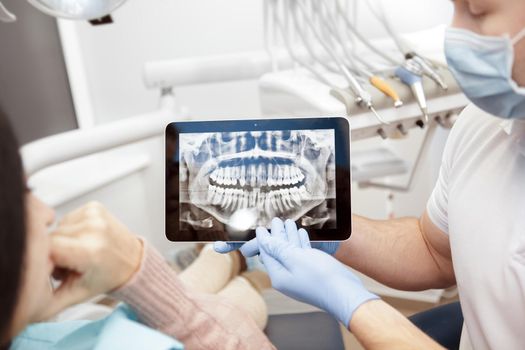 Discussing issues. Cropped shot of a professional dentist showing jaws and teeth x-rays to his patient using a digital tablet technology gadget online issues healthcare medical profession help concept