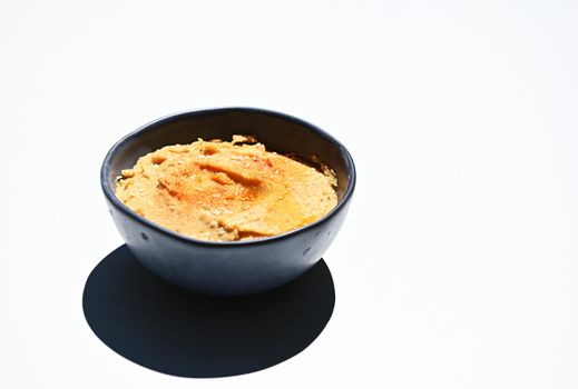 Still life. Blue ceramic bowl of hummus sprinkled with paprika and olive oil, isolated over white background with copy space for advertising text
